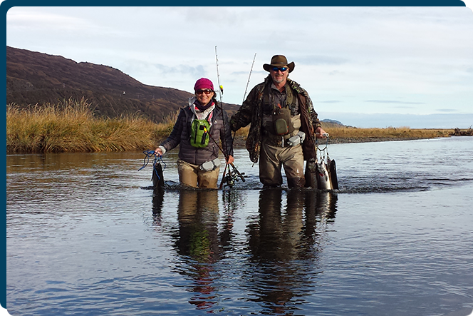 Two people in the water with fishing rods.